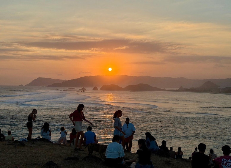 A sunset over a beach with people sitting and standing on the shore. 2