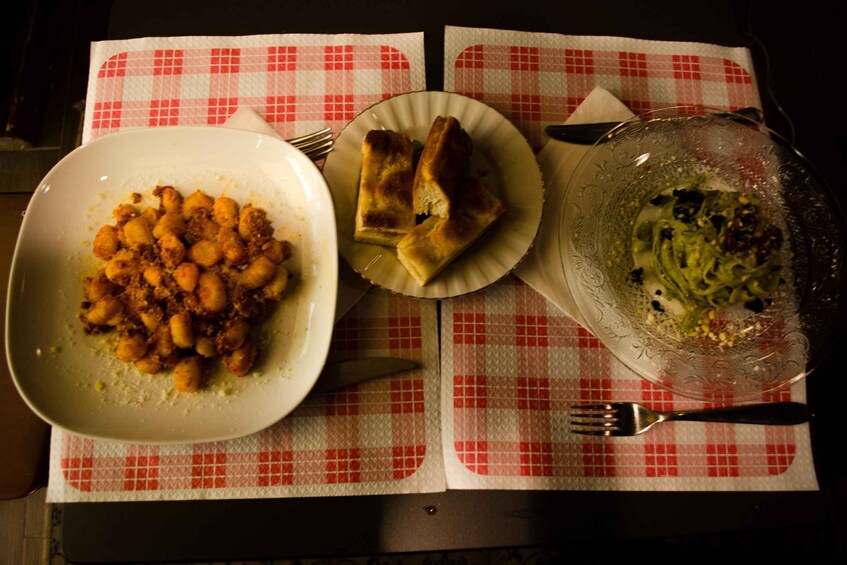 Pöydällä on punavalkoruutuinen pöytäliina, lautasella gnoccheja, toisella lautasella leipää ja kulhossa salaattia. 5