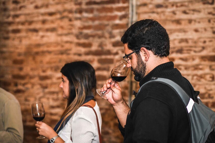 A person holding a wine glass, another person with a wine glass, and a brick wall in the background. 4