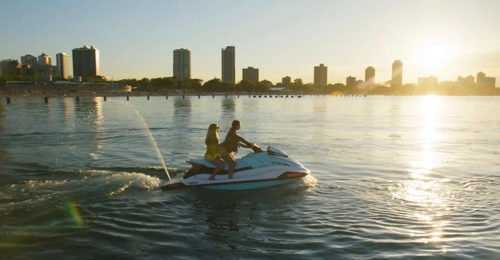 Two people jet skiing on a body of water with a city skyline in the background. 4
