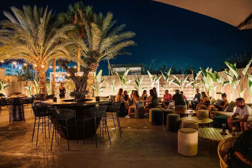 An outdoor seating area with palm trees and tables, surrounded by a bamboo fence. 2
