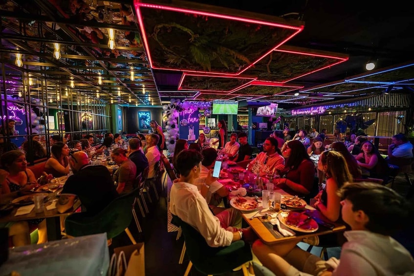 A crowded indoor dining area with neon lights and a vibrant atmosphere. 3