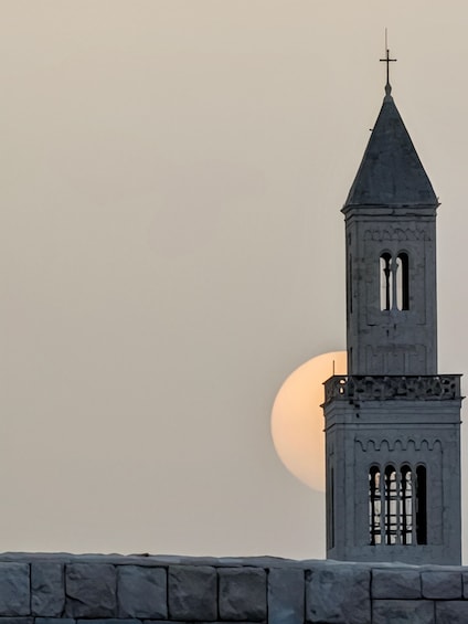 A church tower with a cross on top, set against a backdrop of a large, round moon. 2