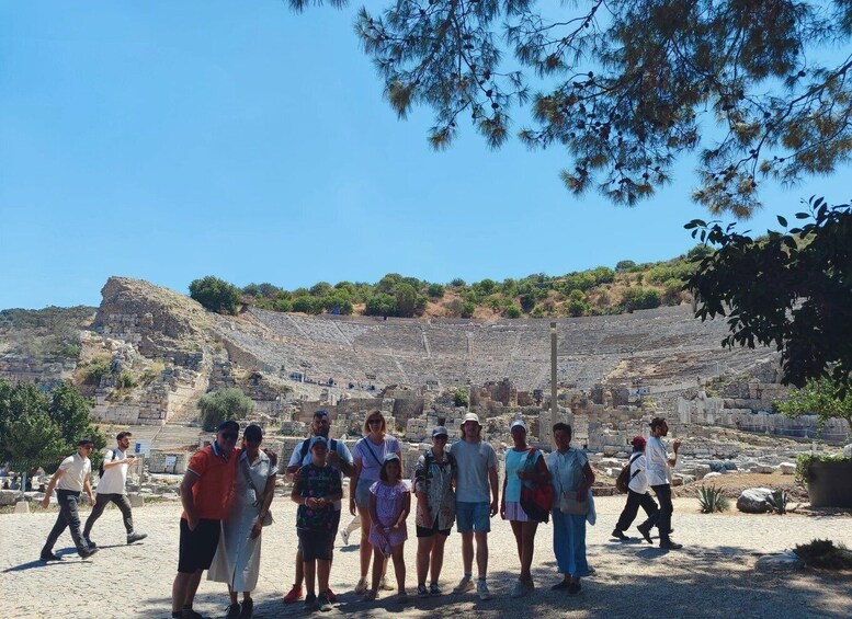 A group of people standing in front of an ancient amphitheater with stone seating and a backdrop of hills. 3