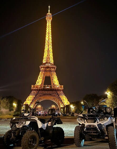 The Eiffel Tower at night, illuminated, with ATVs parked in front. 3