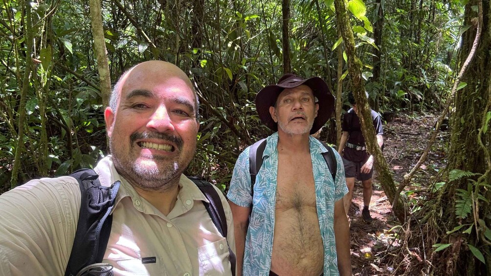 Two people hiking in a dense forest with a variety of green foliage and trees. 4