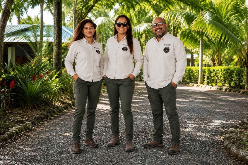 Three people standing on a gravel path surrounded by greenery. 2