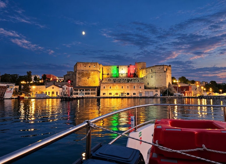 A nighttime view of a historic fortified city with colorful buildings, a calm river, and a boat docked in the foreground. 1