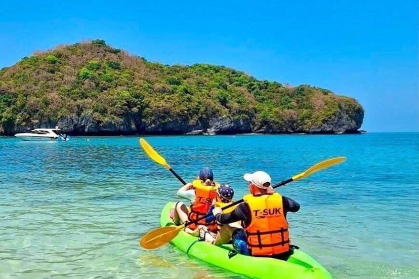 A group kayaking on clear turquoise water with a green kayak, a person wearing a life jacket, and a small island in the background. 5