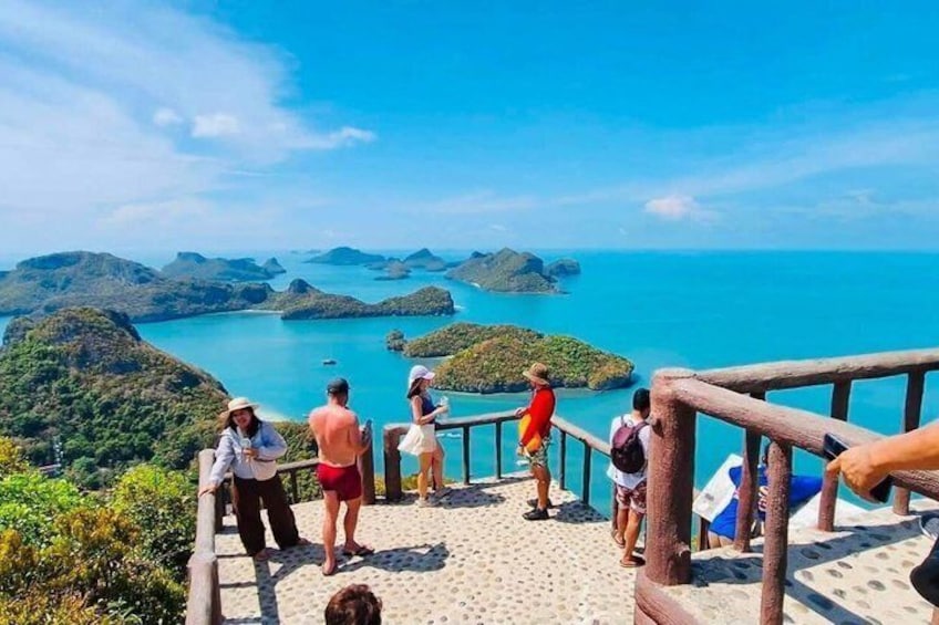 A group of people on a wooden observation deck overlooking a coastal landscape with clear blue waters and green hills. 4
