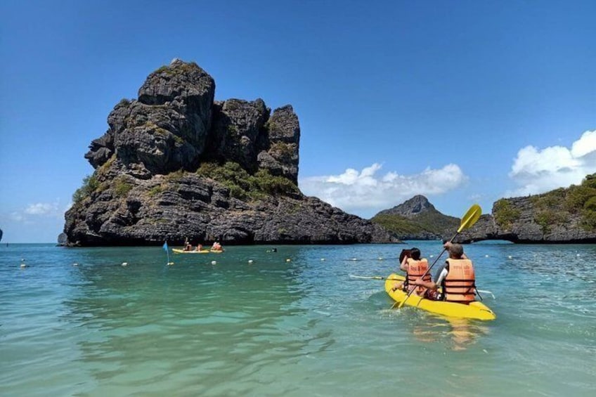Kayakers on a calm sea with a large rock formation in the background. 1