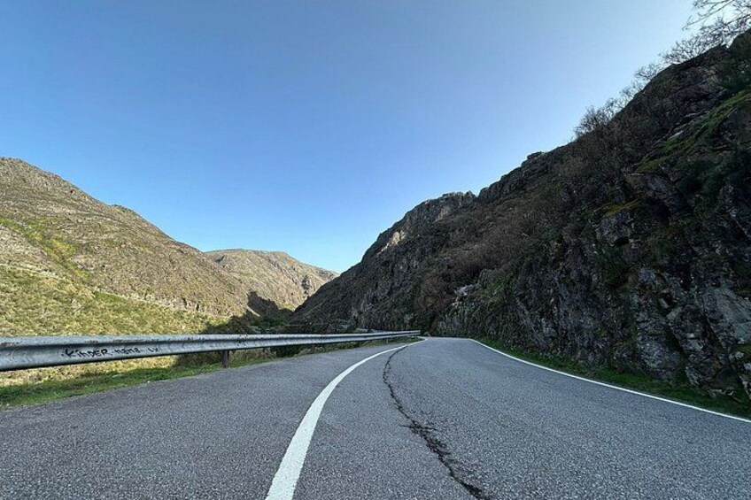 A winding mountain road with guardrails, surrounded by rocky hills and sparse vegetation. 3