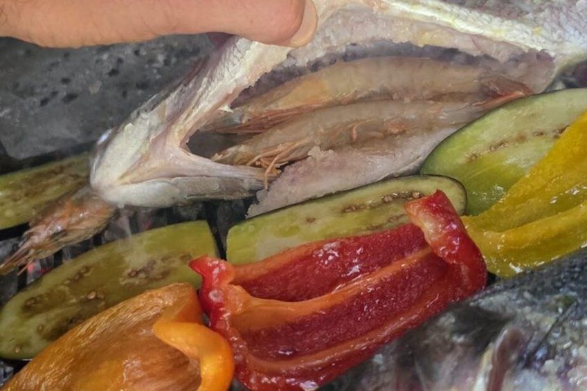 A hand holding a fish, with sliced vegetables and a piece of meat on a grill. 5