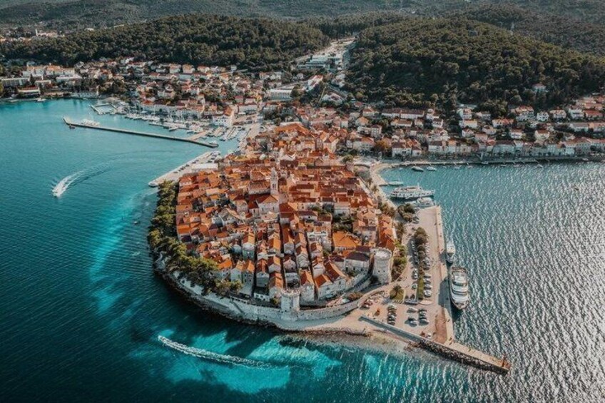 An aerial view of a coastal town with a central island, surrounded by water and a hilly landscape. 1