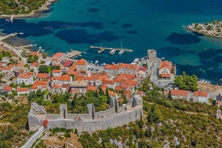 A coastal town with a prominent castle, clear blue waters, and a marina with boats. 5