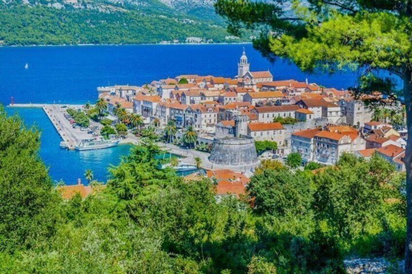 A coastal town with historic buildings, a prominent tower, and a clear blue sea. 1