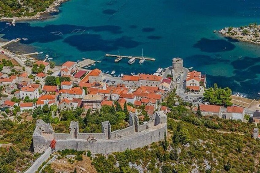 A coastal town with a prominent castle, red-roofed buildings, and clear blue waters. 2