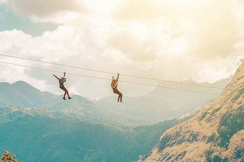 Two people suspended on a cable across a mountainous landscape. 3