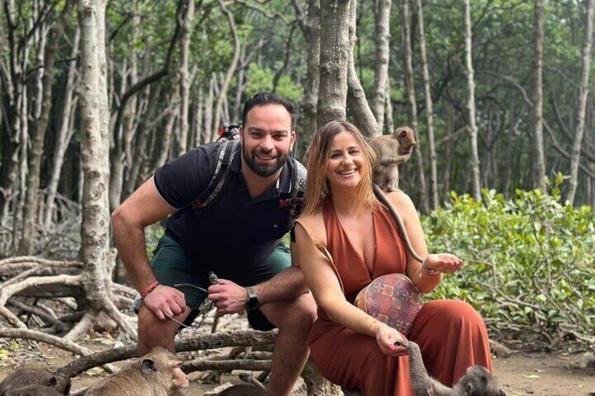 A couple sitting on a fallen tree in a forest with monkeys in the background. 5