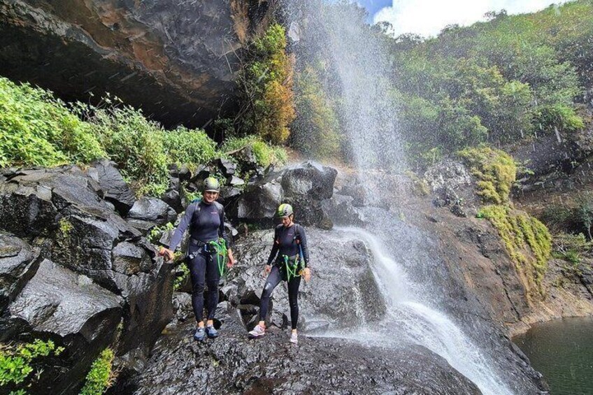 Two people standing on a rocky ledge with a waterfall in the background. 5