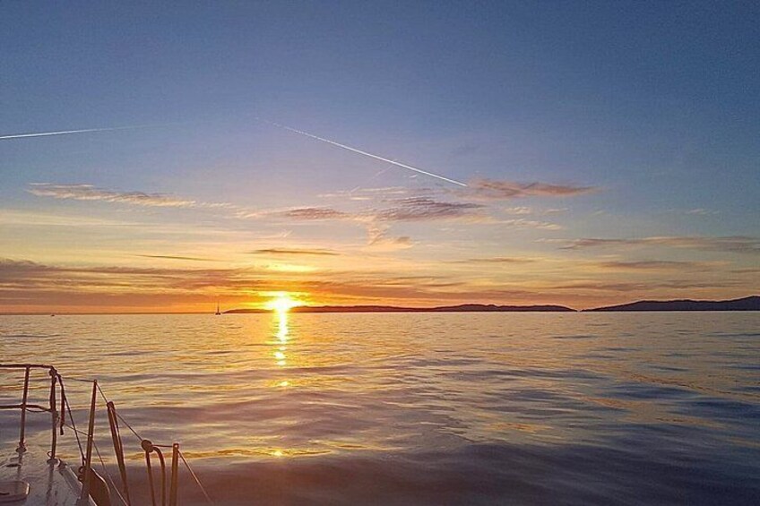 A sunset over a calm sea with a boat in the foreground and distant land on the horizon. 5
