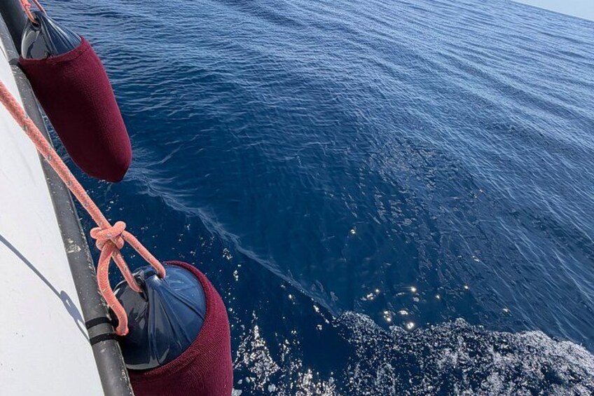 A boat's bow cutting through calm ocean waters, with a red buoy and a rope tied to the side. 3