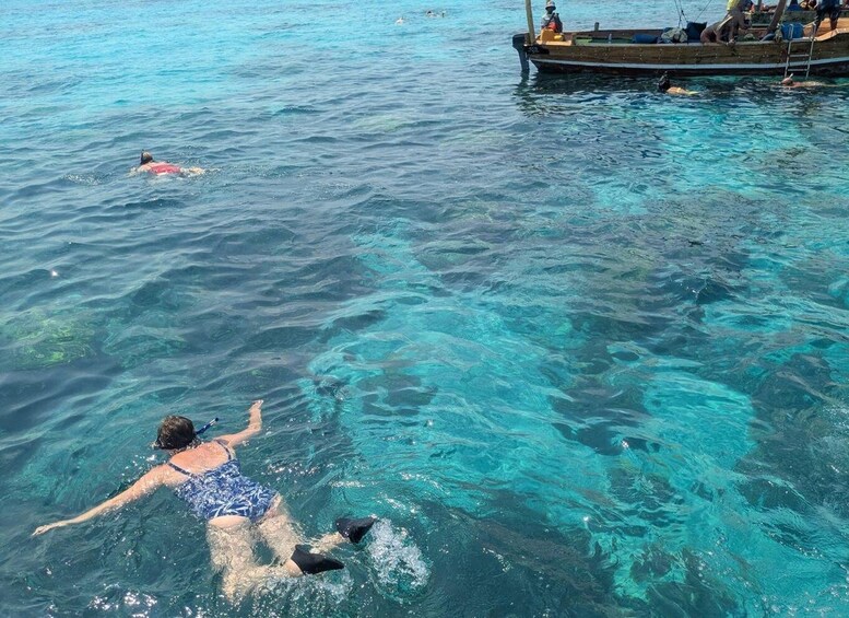 A person swimming in clear blue water with a boat and people in the background. 5
