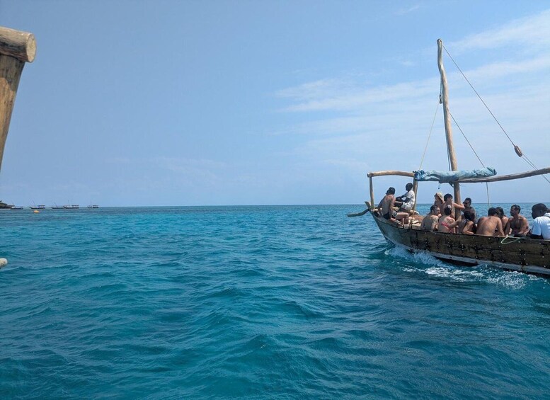 A traditional wooden boat with people on it, floating on calm blue sea water. 5