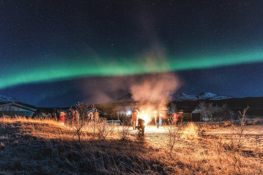 A group of people gathered around a campfire at night, with the Northern Lights in the sky. 4