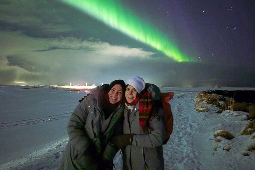 Two people in a snowy landscape with the Northern Lights in the background. 3