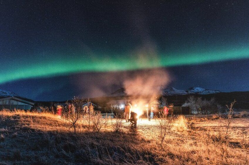 A group of people gathered around a campfire in a snowy landscape with a visible aurora display. 3