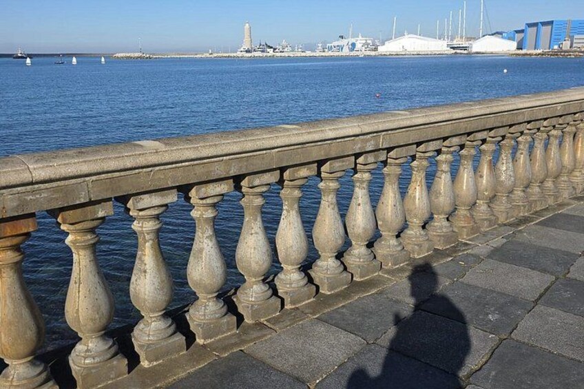 Barandilla de piedra con vistas a un cuerpo de agua con barcos y un horizonte urbano distante. 3
