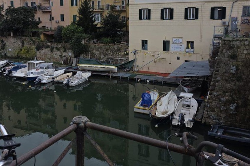 A marina with several boats docked, a building with a sign, and a stone wall. 5