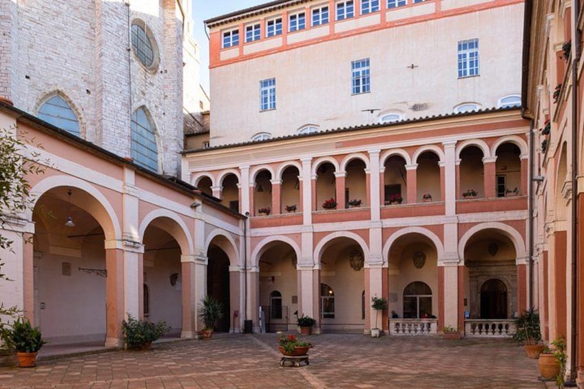 A courtyard with arches, potted plants, and a building with a pink facade. 3