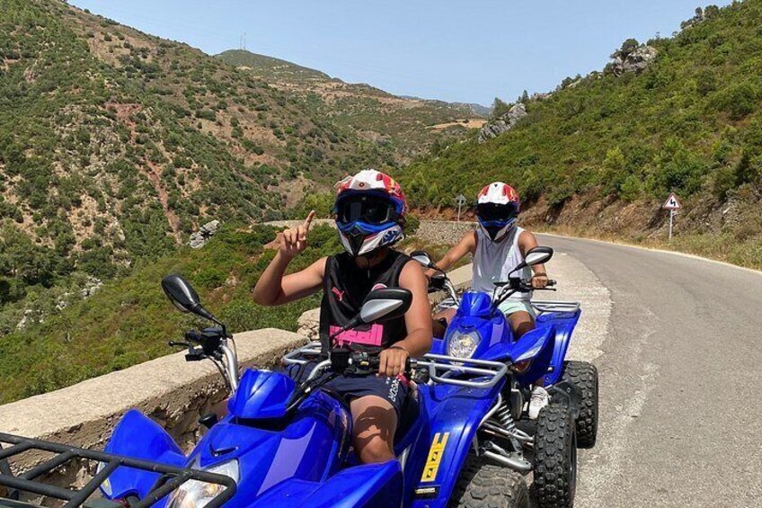 Two people on ATVs on a winding road with a mountainous landscape in the background. 5