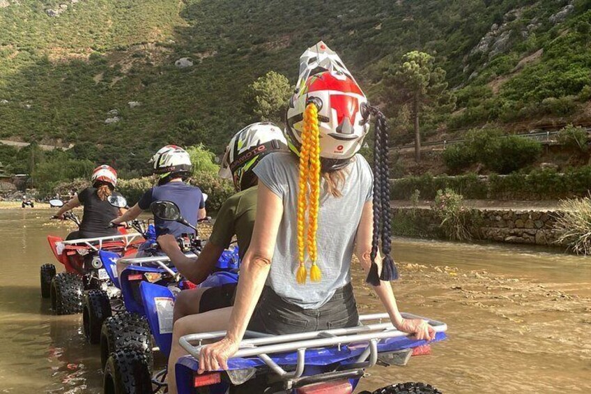 People on quad bikes near a river with a hilly landscape in the background. 4