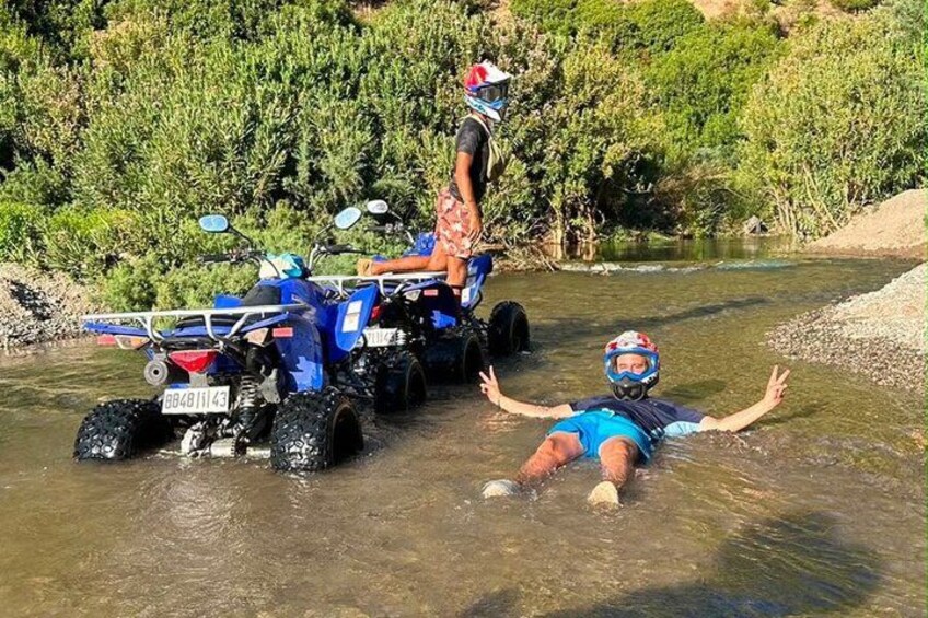 A person in a blue swimsuit and helmet floating in a river with an ATV nearby. 2