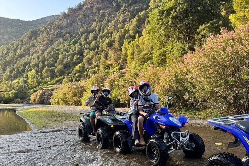 Three people on a blue ATV near a body of water with a forested hillside in the background. 2