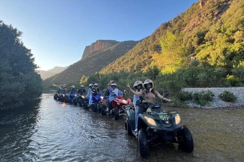 A group of people on quad bikes navigating a river. 4