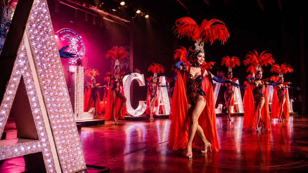 A stage performance with dancers in red costumes and feathered headdresses, illuminated by stage lights. 2