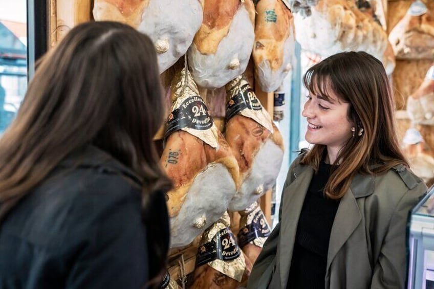Two people in a market, one wearing a green jacket, and various cheeses displayed on shelves. 1