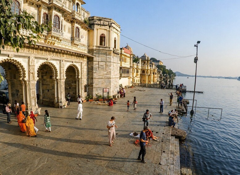A historic building with ornate architecture, a waterfront promenade, and people walking and sitting along the riverside. 4