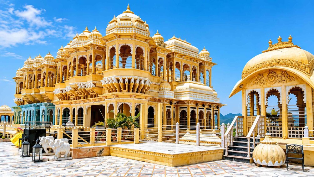 Un edificio grande y ornamentado de color amarillo con múltiples cúpulas y arcos, rodeado por un patio empedrado. 2