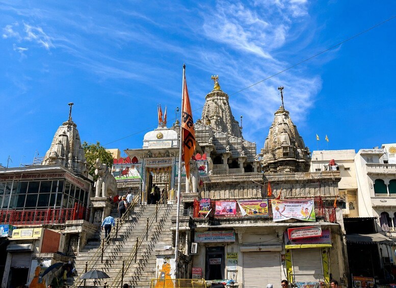 A temple complex with multiple spires and a flagpole, surrounded by shops and a staircase leading to the temple entrance. 3