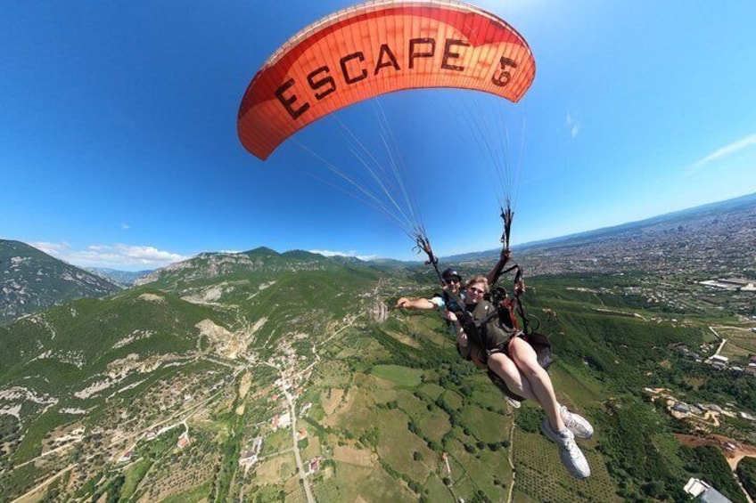 A person paragliding with a parachute labeled 'ESCAPE' over a mountainous landscape. 3