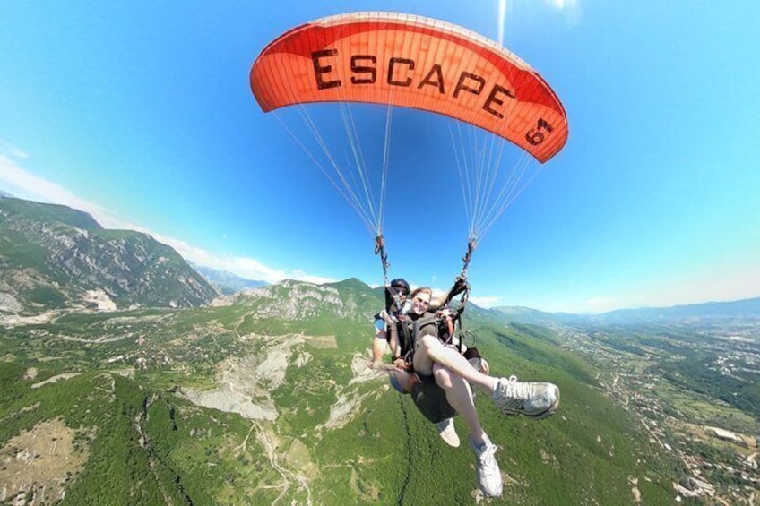 A paraglider with 'ESCAPE' parachute descending over a mountainous landscape. 1