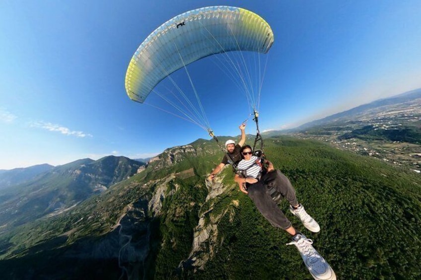A person paragliding over a mountainous landscape with lush greenery and distant city views. 2
