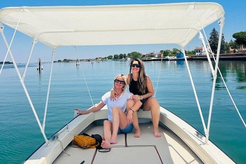 Two people on a boat with a white canopy, water, and distant shoreline with buildings. 5