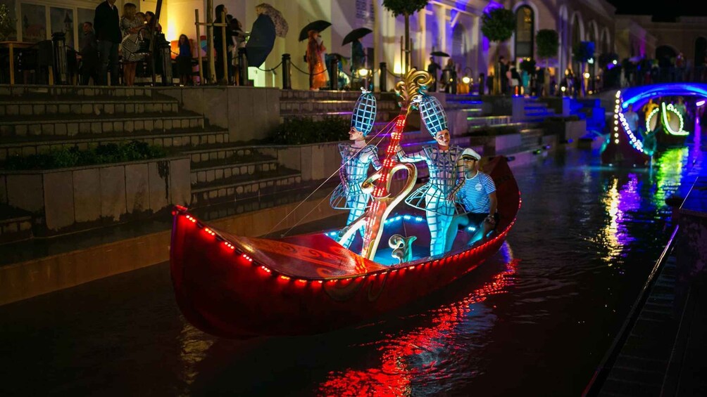 A brightly lit gondola with passengers, illuminated by colorful lights, moving along a canal. 4
