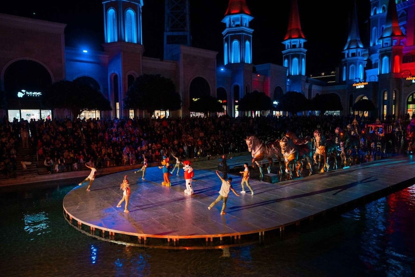 A nighttime outdoor performance on a circular stage with a crowd in the background. 3